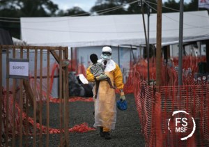 Un trabajador de MSF lleva en brazos a una niña, posible infectada de Ébola, en el centro de MSF de Paynesville, en Liberia. La niña y su madre, ambas con síntomas de la enfermedad, esperaban los resultados de la pruebas. Foto MSF: © John Moore/Getty Images